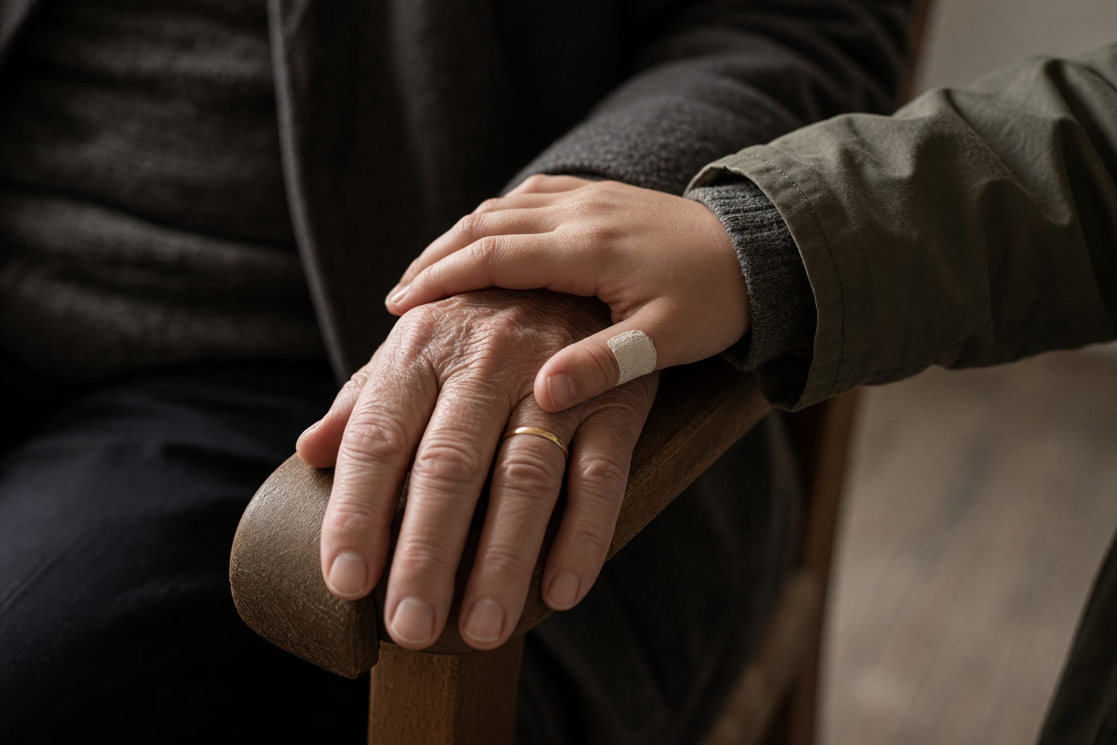 Nahaufnahme der Hände von Grossmutter und Enkelin, die Hand der alten Frau liegt offen, die Hand des Mädchens ruht darauf.